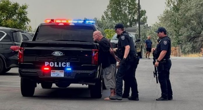 Arrest scene: two police officers detain a barefoot man near a black police pickup with flashing red and blue lights in a parking lot.