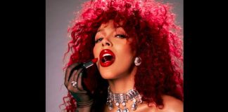 Doja Cat announces Oct. 10 concert stop at Maverik Center Woman with bright red curly hair applying bold red lipstick, wearing diamond earrings and a jeweled choker necklace in a glam portrait.