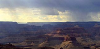 Panoramic view of the Grand Canyon's layered rock formations and deep ravines under a cloudy sky with soft light breaking through clouds.