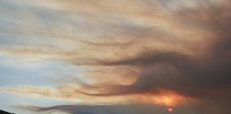 Sunset over rolling hills with orange/pink clouds lit by the setting sun on the horizon, silhouetted hills below