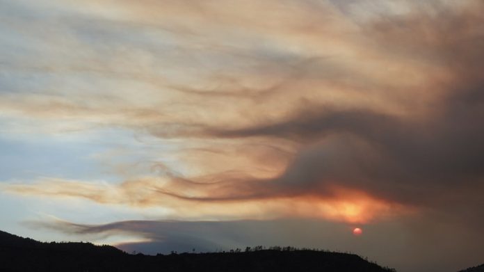 Colorado wildfire Sunset over rolling hills with orange/pink clouds lit by the setting sun on the horizon, silhouetted hills below