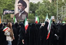 U.S. service members killed in Iran air attack; Trump orders new round of airstrikes in retaliation Crowd of women in black chadors holding Iranian flags at a protest, with a large portrait of a cleric in the background.
