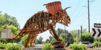 Large rusty metal dragon sculpture on a traffic circle in a suburban street.