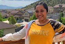 Woman smiling on a wooden balcony overlooking a suburban neighborhood with houses and hills in the distance.