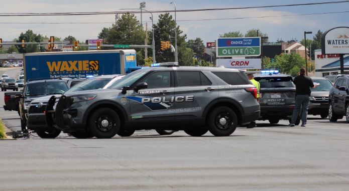 Multiple police SUVs with flashing lights in a parking lot, blocking traffic near a WAXIE truck and stores in the background (police activity scene).