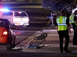Man critically injured when struck by car in Sandy Nighttime street scene of a bicycle crash: toppled bike and debris on the curb, a red car nearby, and officers in reflective vests with a police car flashing in the background.