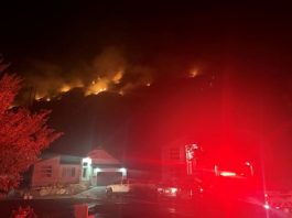 Man, 51, arrested after allegedly starting Ogden’s Mountain Road Fire Nighttime view of a residential neighborhood with a hillside fire and flames above, emergency lights glow red on the scene behind the houses.
