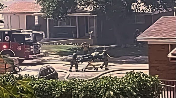 Roy fire Firefighters and bystanders push a stretcher along a suburban street with a fire truck nearby.