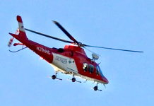 Search underway for missing swimmer at Tibble Fork Reservoir Red-and-white rescue helicopter in flight against a clear blue sky, landing gear visible beneath the fuselage.