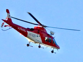 Search underway for missing swimmer at Tibble Fork Reservoir Red-and-white rescue helicopter in flight against a clear blue sky, landing gear visible beneath the fuselage.