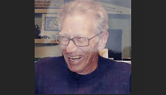 Older man with glasses smiling and laughing, in a dark shirt.