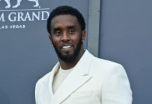 Man in a cream-colored suit posing on a blue-gray backdrop at MGM Grand Las Vegas, smiling for the camera on a red carpet event.