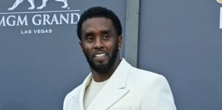 Sean ‘Diddy’ Combs in solitary confinement after prison fight Man in a cream-colored suit posing on a blue-gray backdrop at MGM Grand Las Vegas, smiling for the camera on a red carpet event.