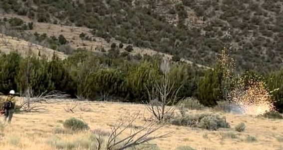 Desert landscape with scrubby bushes and distant hills a person on the left appears to fire with a burst of sparks on the right