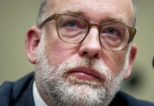 Close-up portrait of a middle-aged man with a gray beard and brown glasses, looking upward thoughtfully.