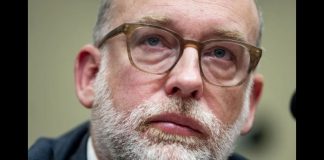 Close-up portrait of a middle-aged man with a gray beard and brown glasses, looking upward thoughtfully.