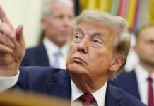 Trump orders Smithsonian to post signs about ‘inaccurate’ history Man in a navy suit raises his index finger while looking upward during a formal meeting; blurred background figures nearby.