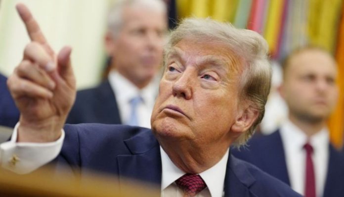 Trump-orders-Smithsonian-to-post-signs-about-inaccurate-history Man in a navy suit raises his index finger while looking upward during a formal meeting; blurred background figures nearby.