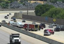 UHP confirms fatal semi-car crash in Taylorsville Emergency responders on a multilane highway incident with fire trucks and police cars, concrete barriers, and houses in the distance on a residential hillside. A signaled lane shows activity and partial closures behind the barrier.