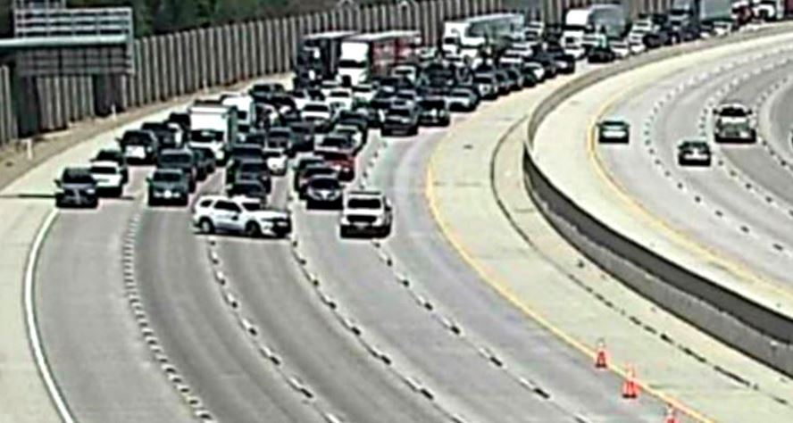 Line of cars stuck in heavy traffic on a curved freeway with orange cones on the right shoulder