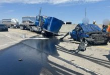 UHP releases details on fatal collision in Taylorsville Wrecked blue semi-truck and a severely damaged car on a highway, with a dark fluid spill and responders nearby under a clear sky.
