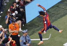 Soccer player in Barcelona kit leaps over sideline barrier as photographers capture the moment from the crowd.