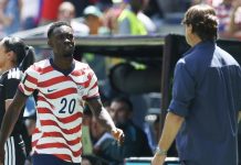 USA team eliminated from World Cup competition; Belgium dominates USMNT in 4-1 rout Soccer player wearing a red-and-white striped USA jersey with number 20 walks toward the sideline, with a man in a blue shirt nearby.