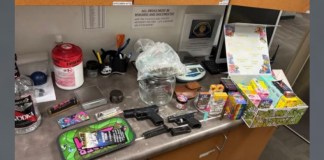 Evidence on a lab counter: two handguns, a bottle of vodka, drugs and packaging, scales and small tools among miscellaneous items.
