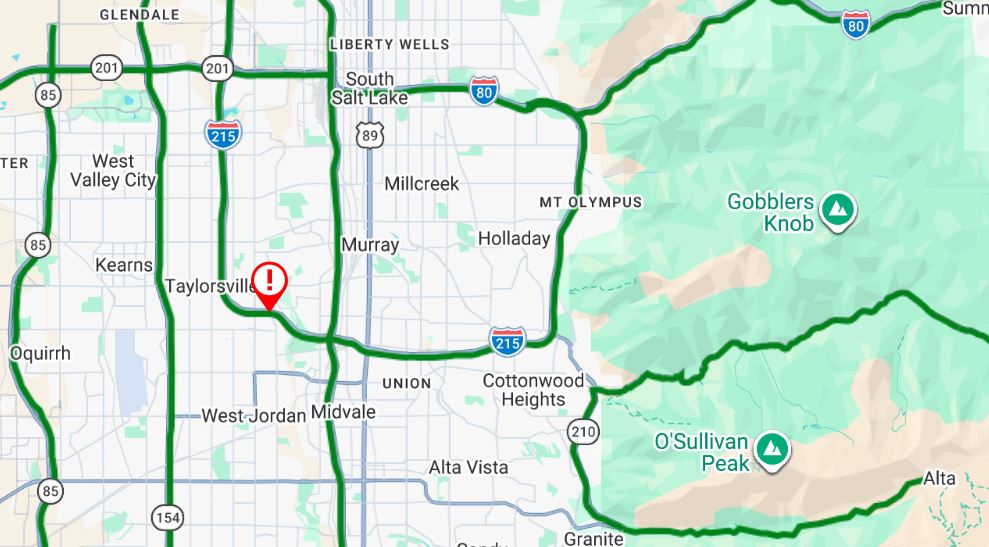 Map showing a traffic incident west of Taylorsville Utah with a red pin and exclamation mark on a highway near I 215 nearby I 80 and surrounding mountains are visible